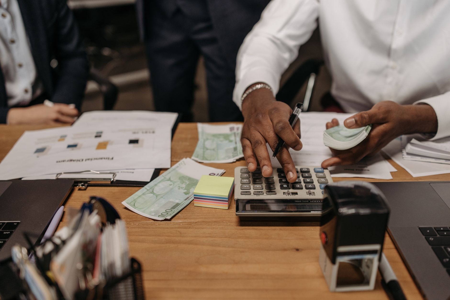 Person arbejder med regnskab, lommeregner og kontanter ved et skrivebord